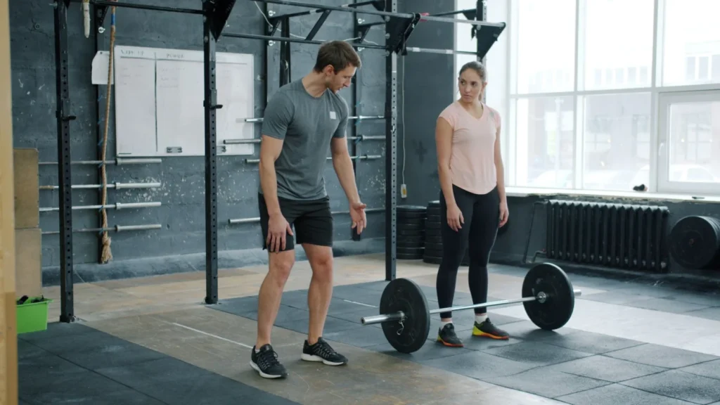 A personal trainer instructing a woman on barbell lifting technique in a gym setting.