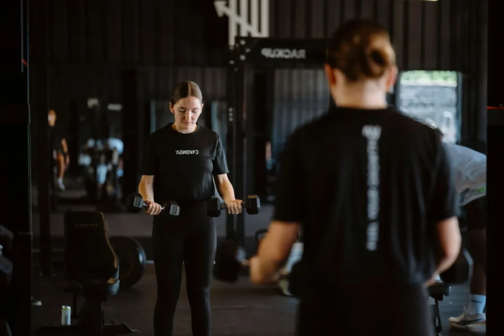 A woman performing a focused dumbbell workout in a modern gym setting.