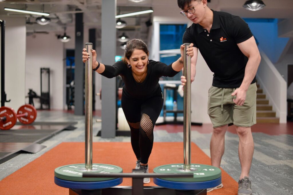 Person using cable machine with trainer supervision