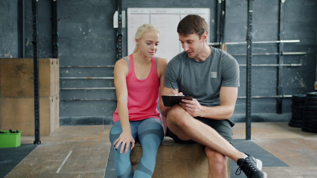Experienced fitness coach observing client workout in gym