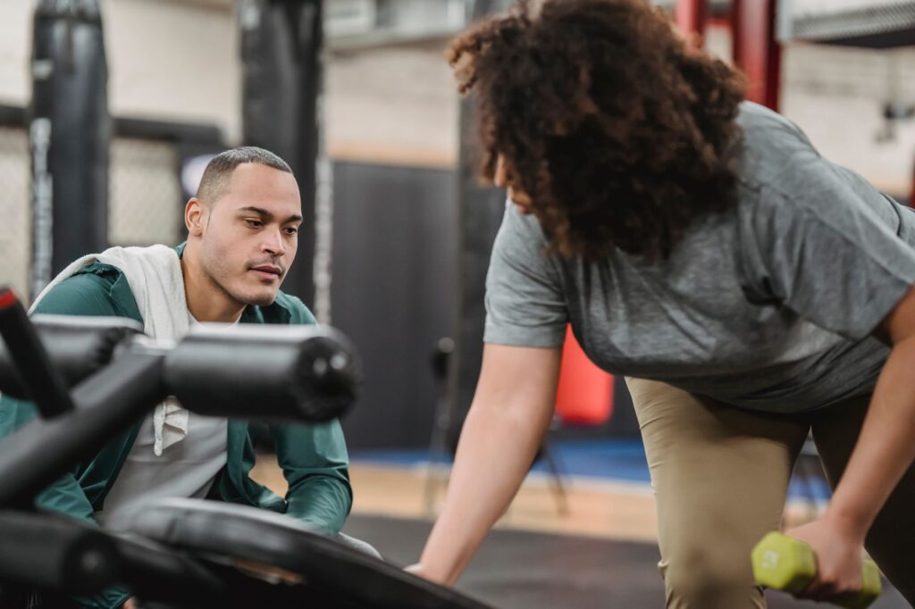 Trainer spotting client during barbell exercise at gym